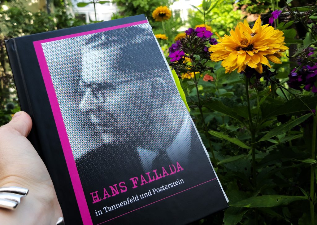 Jemand hält das Buch "Hans Fallada in Tannenfeld und Posterstein" in Falladas Garten in Carwitz