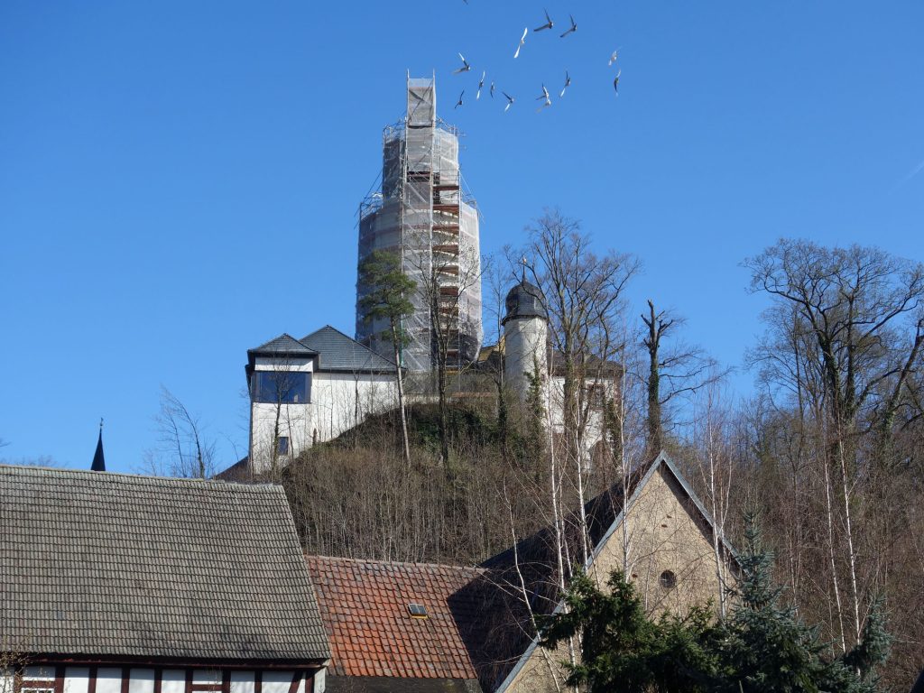 Blick vom Dorf den Berg hinauf auf die Steilseite der Burg, man sieht den Erker des Nordflügels mit großen Glasfenstern