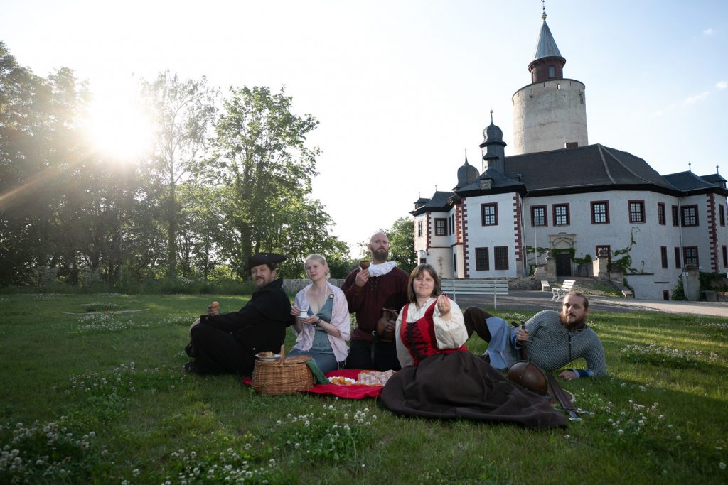Fünf Leute aus verschiedenen Zeiten beim gemeinsamen Picknick vor der Burg Posterstein. Mit Genuss durch die Jahrhunderte - in dieser Führung geht es ums Essen (Foto: Ronny Ristok, Gefolgschaft zu Posterstein)