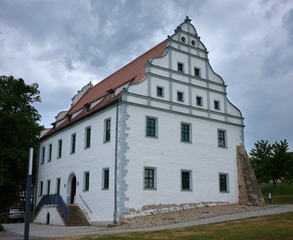 Das Herrenhaus Oberzetzscha hat einen wellenförmigen Giebel und ist weiß verputzt mit grauen Eckquaderungen.